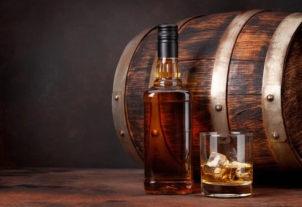 A bottle of whiskey and two glasses on top of a barrel.